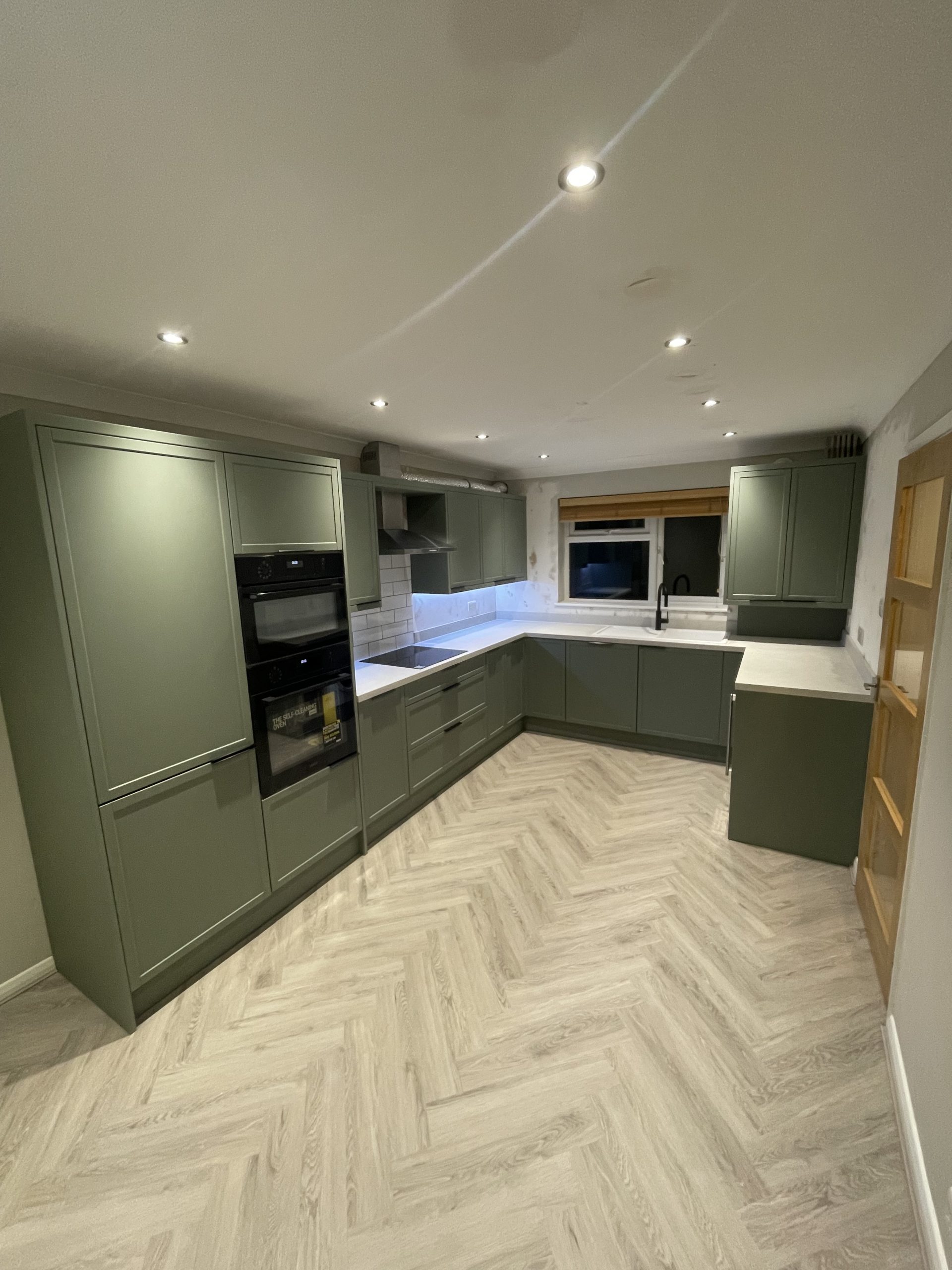 L-shaped kitchen fitting Reading with sage cabinets and herringbone flooring